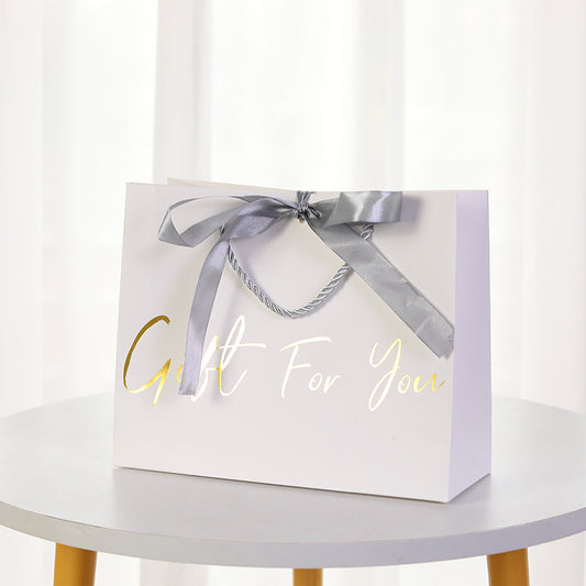 Kraft paper gift bag with twisted metal rope handle and satin bow on a neutral background