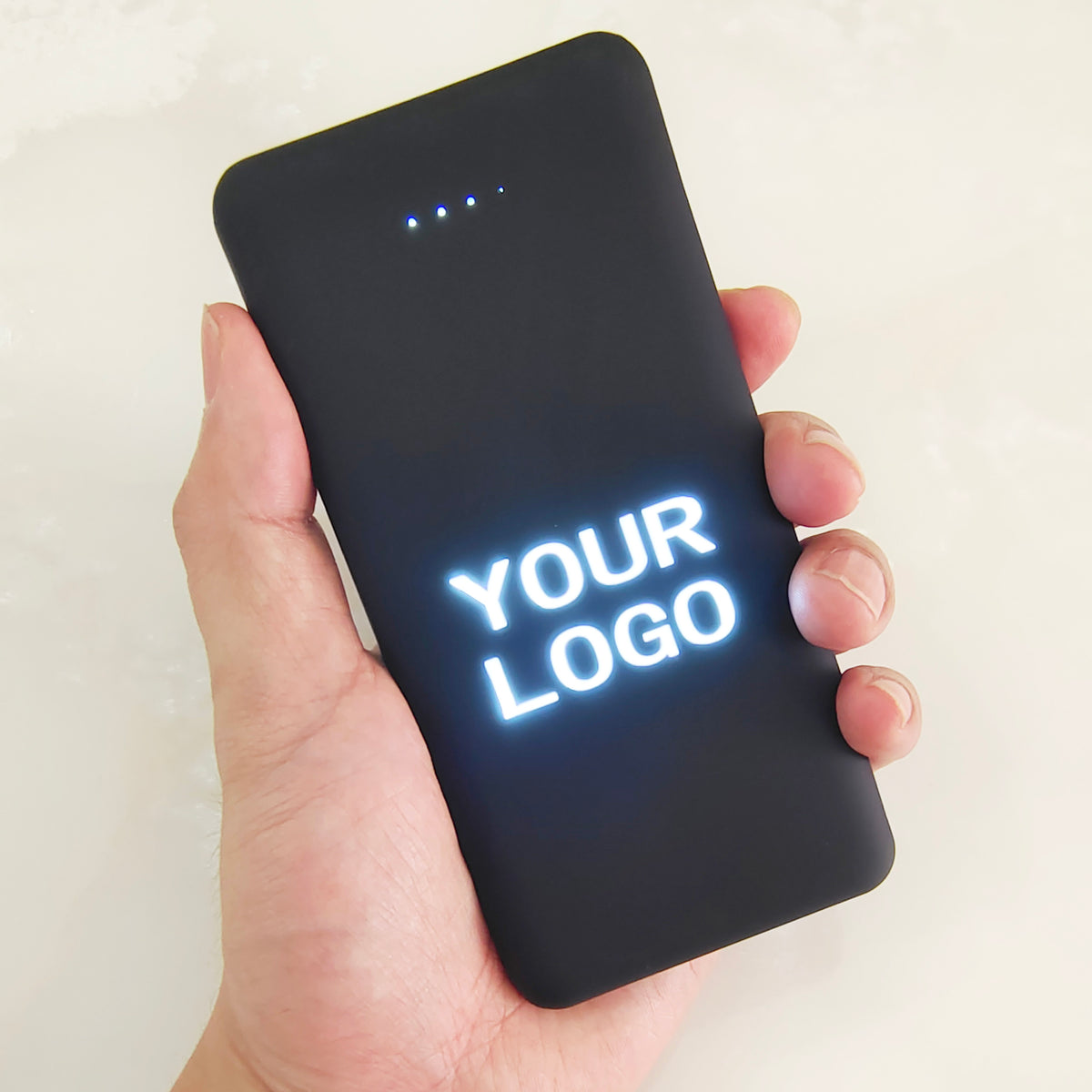 Black rectangular power bank with glowing LED logo panel and multiple USB ports on a dark surface