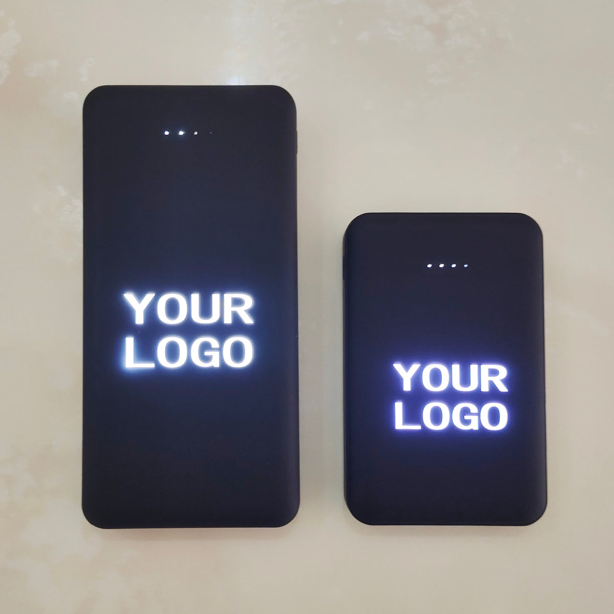 Angled close-up of black rectangular power bank with LED logo lit and USB ports visible